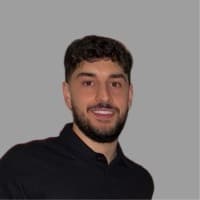 Smiling man with dark curly hair and a beard, wearing a black polo shirt.